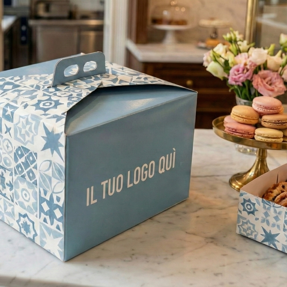Dettaglio di una scatola a bauletto professionale per colombe e dolci con trama a maioliche blu e bianche e spazio per logo personalizzato su bancone in marmo.